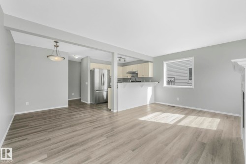 The property features light-colored flooring, a kitchen with a stainless steel refrigerator, and a window providing natural light - 123 230 Edwards Drive, Edmonton, AB - Indoor Photo Showing Other Room
