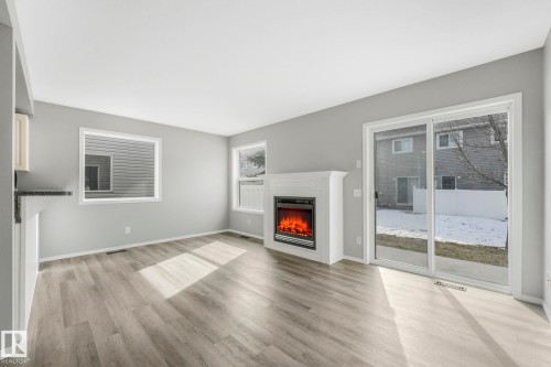 Living area featuring light-colored flooring, a fireplace with a white mantel, and sliding glass doors providing outdoor access - 123 230 Edwards Drive, Edmonton, AB - Indoor Photo Showing Living Room With Fireplace