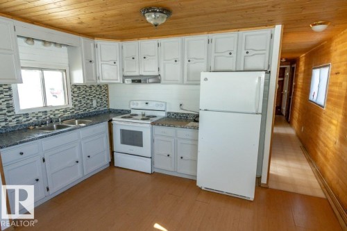 The kitchen features white cabinetry, a double basin sink, and a mosaic tile backsplash - 112, 57004 Range Rd 105, Rural St. Paul County, AB - Indoor Photo Showing Kitchen With Double Sink