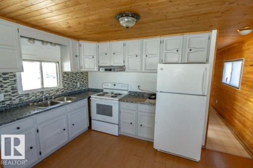 The kitchen features white cabinetry, a double basin sink, a white range, a white refrigerator, and a wood plank ceiling - 112, 57004 Range Rd 105, Rural St. Paul County, AB - Indoor Photo Showing Kitchen With Double Sink