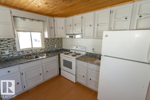 The property features a kitchen with white cabinetry, a double basin sink, and mosaic tile backsplash - 112, 57004 Range Rd 105, Rural St. Paul County, AB - Indoor Photo Showing Kitchen With Double Sink