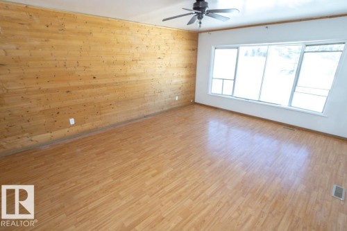 This expansive room features light wood flooring, a striking wood-paneled accent wall, and a large window offering natural light - 112, 57004 Range Rd 105, Rural St. Paul County, AB - Indoor Photo Showing Other Room