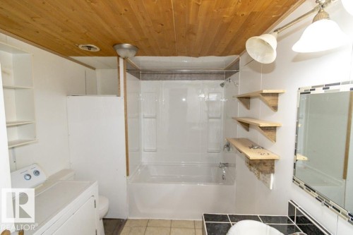 The bathroom features a bathtub with a shower, a vanity with a mirror, and a wood plank ceiling - 112, 57004 Range Rd 105, Rural St. Paul County, AB - Indoor Photo Showing Bathroom