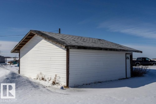 The property includes a white sided outbuilding with a dark shingle roof, set against a clear blue sky - 112, 57004 Range Rd 105, Rural St. Paul County, AB - Outdoor