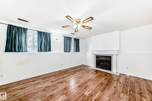 The property features a room with wood-look flooring, a white mantel fireplace, and a ceiling fan with integrated lighting - 1832 42 Street, Edmonton, AB - Indoor Photo Showing Living Room With Fireplace