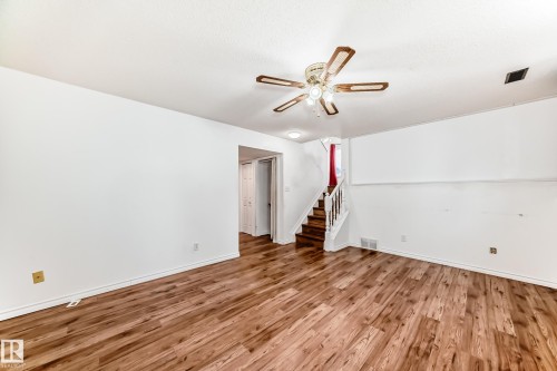 Spacious room featuring wood-look flooring, a ceiling fan with integrated lighting, and a staircase with a white railing - 1832 42 Street, Edmonton, AB - Indoor Photo Showing Other Room