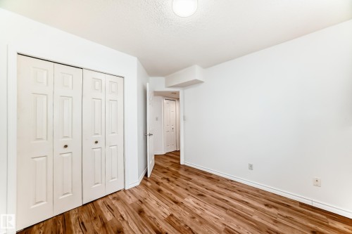 The room features bright white walls, warm-toned wood flooring, and white bi-fold closet doors - 1832 42 Street, Edmonton, AB - Indoor Photo Showing Other Room