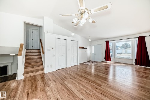 Bright living space featuring hardwood style flooring, a bay window with red drapes, and a ceiling fan with integrated lighting - 1832 42 Street, Edmonton, AB - Indoor With Fireplace