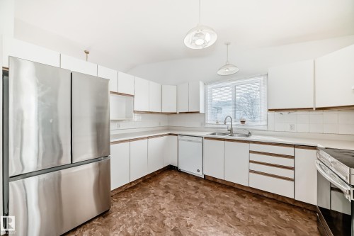 The kitchen features white cabinetry, a stainless steel refrigerator, and a window with blinds providing natural light - 1832 42 Street, Edmonton, AB - Indoor Photo Showing Kitchen With Double Sink
