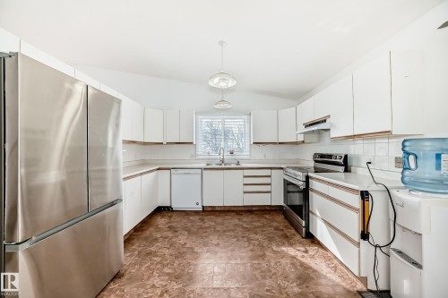 The property features a kitchen with white cabinetry, a stainless steel refrigerator, an oven, and a dishwasher - 1832 42 Street, Edmonton, AB - Indoor Photo Showing Kitchen