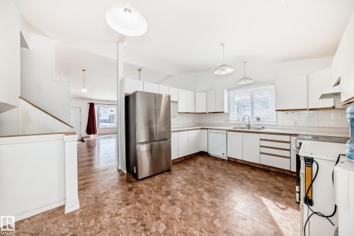 The kitchen features white cabinetry, a stainless steel refrigerator, and a window above the sink - 1832 42 Street, Edmonton, AB - Indoor Photo Showing Kitchen