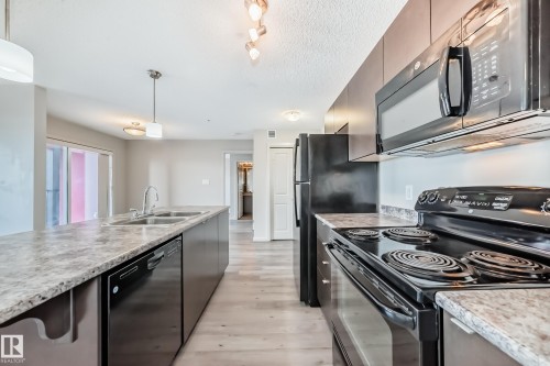 The kitchen features black appliances, including a microwave, oven, and refrigerator - 332 344 Windermere Road, Edmonton, AB - Indoor Photo Showing Kitchen With Double Sink