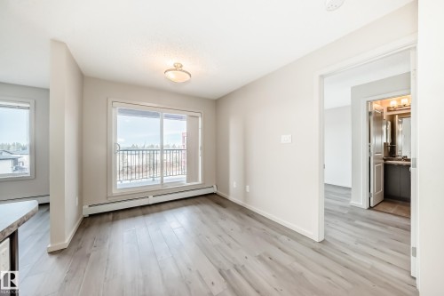 Living area featuring light-toned flooring, a sliding glass door providing access to an outdoor space, and white baseboard heating - 332 344 Windermere Road, Edmonton, AB - Indoor Photo Showing Other Room