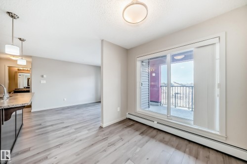 The property features light wood flooring, neutral colored walls, and a glass sliding door that opens to a balcony with black metal railings - 332 344 Windermere Road, Edmonton, AB - Indoor Photo Showing Other Room
