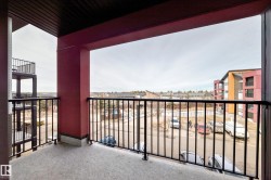 This property features a balcony with a concrete floor, dark metal railings, and a red exterior wall, offering views of residential buildings and vehicles - 