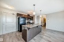 The kitchen features dark wood cabinetry, a black refrigerator, a black oven, and a kitchen island with a sink and pendant lighting - 332 344 Windermere Road, Edmonton, AB  - Indoor Photo Showing Kitchen With Double Sink 