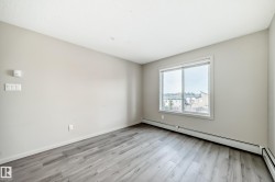 Bright interior space featuring light-colored walls, wood-look flooring, and a window providing views of nearby structures and trees - 
