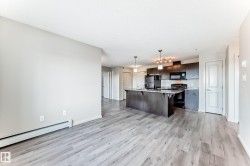 Open concept living space featuring light-toned flooring, a kitchen island with seating, dark cabinetry, and integrated appliances - 