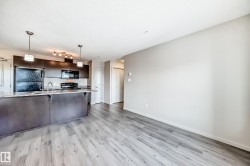 Open concept living area featuring light-toned flooring and a kitchen with dark cabinetry and a light-colored countertop - 