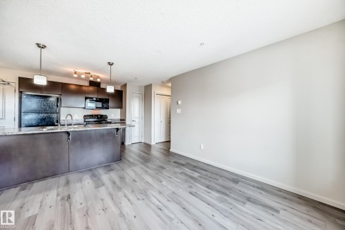 Open concept living area featuring light-toned flooring and a kitchen with dark cabinetry and a light-colored countertop - 332 344 Windermere Road, Edmonton, AB - Indoor Photo Showing Kitchen