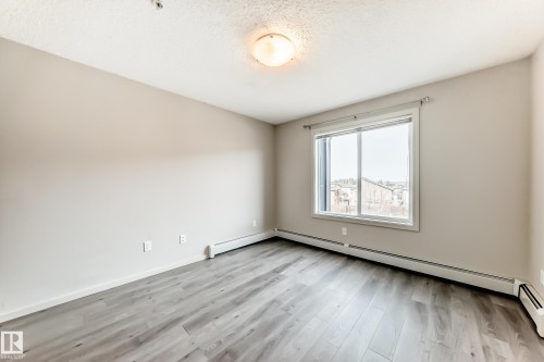 This room features light grey walls, grey wood-style flooring, and a window with a view of other properties - 332 344 Windermere Road, Edmonton, AB - Indoor Photo Showing Other Room
