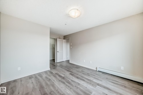 This room features light grey walls, grey plank flooring, and a ceiling light fixture - 332 344 Windermere Road, Edmonton, AB - Indoor Photo Showing Other Room