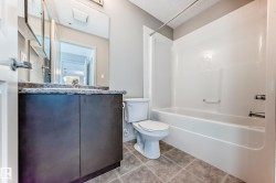 Bathroom featuring a dark wood vanity with a light-colored countertop, a white toilet, and a white bathtub with a shower - 