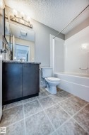Bathroom featuring a vanity with dark cabinetry and a light-colored countertop, a toilet, and a white bathtub with a shower rod - 
