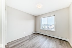 This room features gray wood-look flooring, light-colored walls, and a large window providing views of nearby structures and trees - 