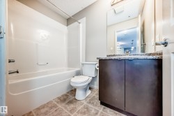 Bathroom featuring a built-in bathtub with shower, a vanity with a dark wood cabinet and stone countertop, and tiled flooring - 