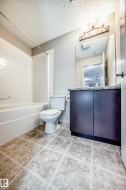 Bathroom featuring a white bathtub, toilet, and a vanity with a mirror and light fixture - 