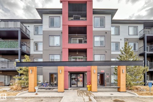 The property features a multi-story exterior with a modern design, incorporating grey and red panels, and numerous balconies with black railings - 332 344 Windermere Road, Edmonton, AB - Outdoor With Balcony With Facade