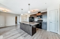 The kitchen features dark cabinetry, black appliances, and a central island with a sink and stone-look countertop - 