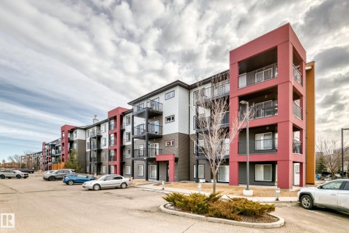 The property is a contemporary multi-story building featuring a distinct red, white, and grey exterior, with dark-framed windows and balconies with glass and black railings - 332 344 Windermere Road, Edmonton, AB - Outdoor With Balcony With Facade