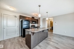 The kitchen features dark wood cabinetry, a black refrigerator, a black oven, and a kitchen island with a sink and pendant lighting - 