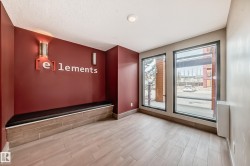 This space features large windows providing views of the outdoors, a built-in bench with a black cushion, and light-colored plank flooring - 