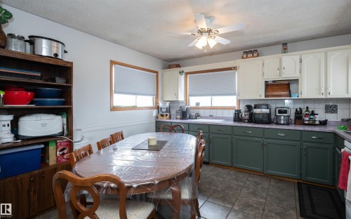 The kitchen features white upper cabinetry, dark green lower cabinetry, and a tiled backsplash - 4420 56 Avenue, Barrhead, AB - Indoor