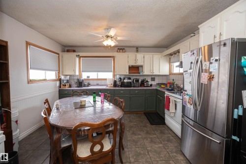 The kitchen features a dining area with a wooden table, tiled flooring, and windows with blinds - 4420 56 Avenue, Barrhead, AB - Indoor
