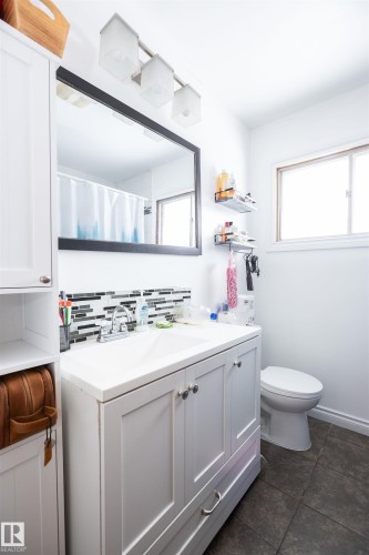 Well-appointed bathroom featuring a vanity with a white countertop and base cabinets, a wall-mounted mirror, and dark tile flooring - 4420 56 Avenue, Barrhead, AB - Indoor Photo Showing Bathroom