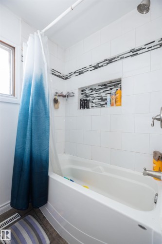 The bathroom features a white bathtub and white tiled walls, accented with a decorative tile border - 4420 56 Avenue, Barrhead, AB - Indoor Photo Showing Bathroom