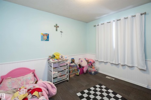 The room features light blue walls with white wainscoting, dark flooring, and a window with white curtains - 4420 56 Avenue, Barrhead, AB - Indoor Photo Showing Bedroom