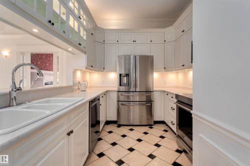 The kitchen features white cabinetry, stainless steel appliances, a double basin sink, and a black and white tiled floor - 102 11826 100, Edmonton, AB - Indoor Photo Showing Kitchen With Double Sink With Upgraded Kitchen