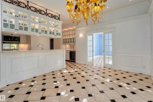 Expansive kitchen and dining area featuring a black and white tiled floor, white cabinetry, a built-in microwave, and a gold chandelier - 102 11826 100, Edmonton, AB - Indoor Photo Showing Other Room