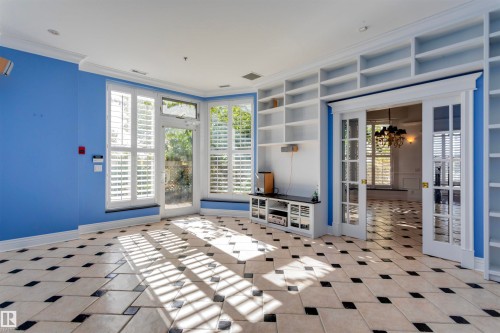 This bright room features patterned tile flooring, extensive built-in shelving, and several windows with plantation shutters that allow natural light to fill the space - 102 11826 100, Edmonton, AB - Indoor Photo Showing Other Room