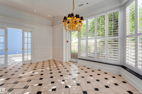 This room features a striking black and tan tiled floor, a decorative gold chandelier with black shades, and a series of large windows with white louvered shutters - 102 11826 100, Edmonton, AB - Indoor Photo Showing Other Room