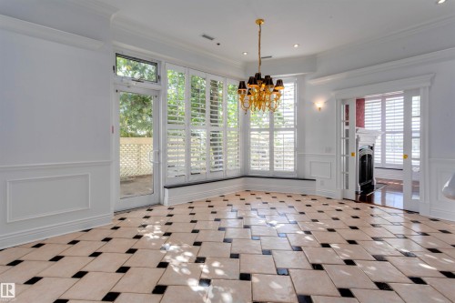 This room features a striking tile floor with a geometric pattern, wall paneling, and an ornate chandelier - 102 11826 100, Edmonton, AB - Indoor Photo Showing Other Room
