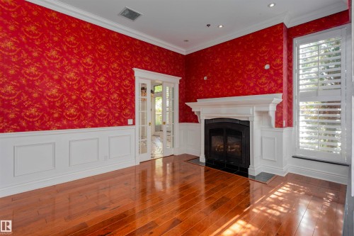 Spacious room featuring hardwood floors, a fireplace with a white mantel, and red patterned walls with white wainscoting - 102 11826 100, Edmonton, AB - Indoor With Fireplace