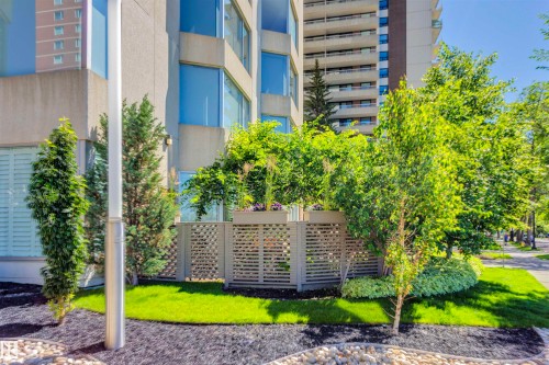 Well-maintained landscaping featuring lush green lawn, mature trees, and decorative planters, complementing the building's exterior - 102 11826 100, Edmonton, AB - Outdoor