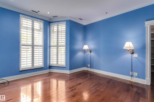 This room features hardwood floors, two windows with white plantation shutters, and two wall-mounted sconces - 102 11826 100, Edmonton, AB - Indoor Photo Showing Other Room
