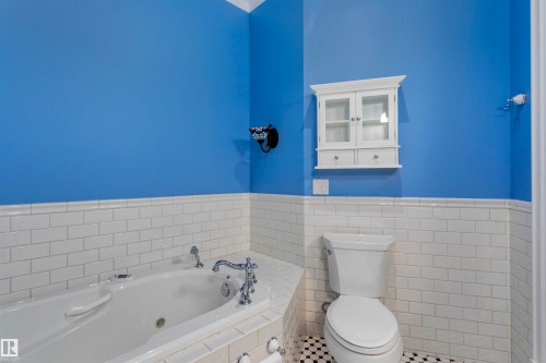Bathroom featuring a white built-in tub with chrome fixtures, subway tile wainscoting, and a wall-mounted storage cabinet - 102 11826 100, Edmonton, AB - Indoor Photo Showing Bathroom